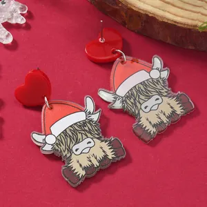 Close-up of cute acrylic Christmas earrings featuring Highland cows with festive red hats