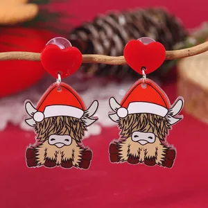 Detailed shot of Christmas highland cow acrylic earrings hanging on a rustic wooden branch