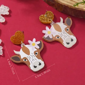 Macro shot of cartoon cow acrylic earrings with size labels and festive gold glitter heart