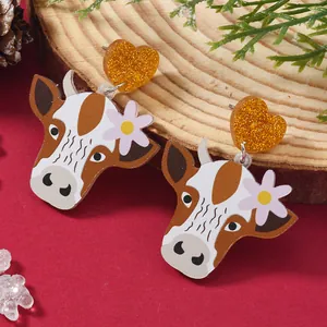 Cute acrylic cow earrings with glitter heart studs and floral detail on festive wood background