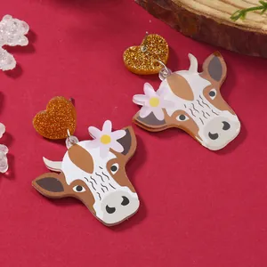 Cute acrylic cow earrings with gold glitter heart studs on a festive red background
