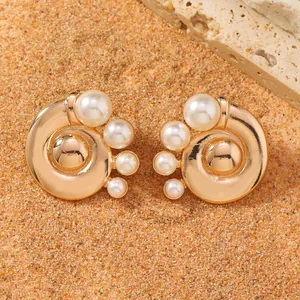 Boucles spirales dorées avec perles blanches sur sable orange et pierre