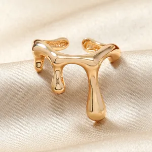 Détail d'une bague dorée forme goutte fluide sur fond de soie plissée beige