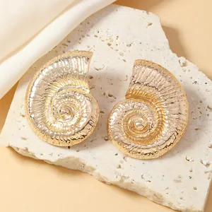 Dettaglio orecchini a spirale a forma di nautilus dorati su superficie in pietra ruvida