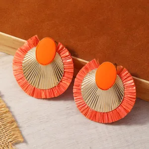 Dettaglio orecchini con nappe in rafia arancione con disco dorato e resina ovale