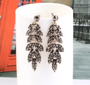 Detailed close-up of dark grey zircon leaf drop earrings on a white stand with street background