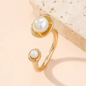 Close-up of adjustable gold ring featuring dual pearls on a textured stone surface