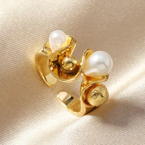 Detail of gold open ring featuring white pearls and a textured metal ball on satin