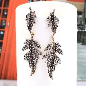 Close-up of vintage dark gold leaf drop earrings with grey rhinestones on a white stand