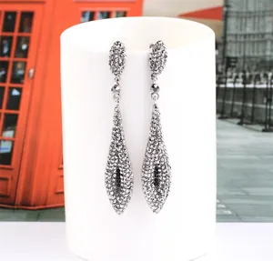 Detailed view of silver long drop earrings with black stones and crystals on a white stand