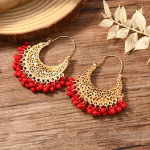 Detail view of gold-plated crescent earrings with red bead fringes and filigree metalwork