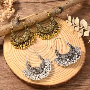Close-up of vintage hollow hoop earrings with metal bead fringe on a rustic wood tray