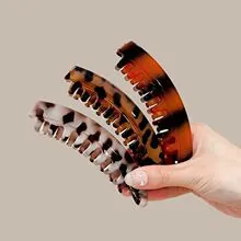 Detail view of three leopard and tortoiseshell patterned hair clips held in hand