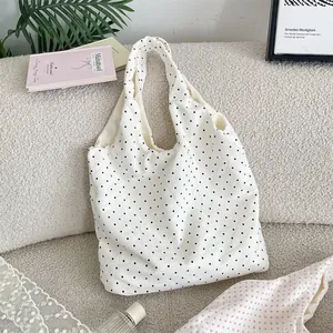 White canvas tote bag with black polka dots displayed in a lifestyle setting on a sofa.