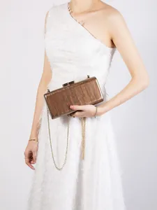 Brown wood-textured acrylic clutch bag with gold chain strap on white feather dress