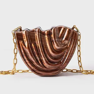 Detail of shell-shaped brown acrylic evening bag with gold chunky chain strap