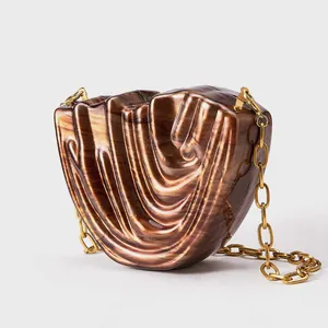 Macro view of wave-shaped acrylic evening clutch with amber marble texture and gold chain