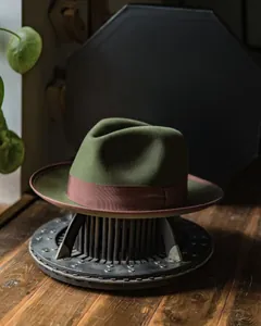 Detail of dark green wool felt fedora hat featuring a brown satin ribbon on a metal stand