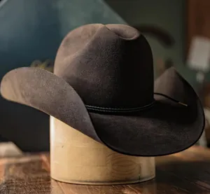 Detalle de sombrero vaquero de fieltro marrón oscuro con banda trenzada en soporte de madera