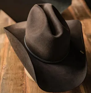 Primer plano de sombrero cowboy de fieltro marrón con cordón trenzado sobre madera rústica