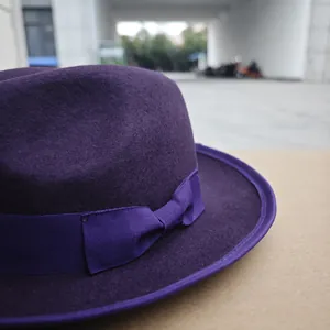 Detail of a dark purple wool fedora hat featuring a matching grosgrain ribbon and bow