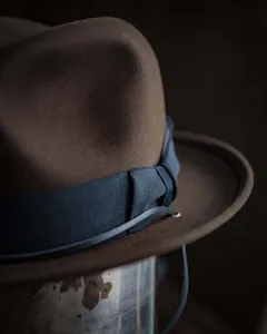 Macro shot of dark brown wool fedora hat featuring blue ribbon and metal eyelet detail
