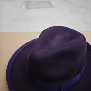Detail of dark purple wool fedora hat featuring a ribbed ribbon and classic indented crown