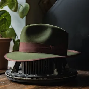 Olive green wool felt Panama hat with dark brown ribbon trim on a vintage display stand
