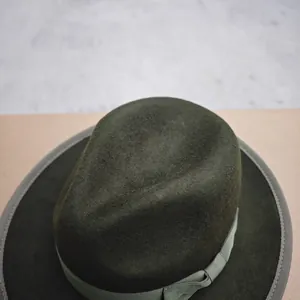 Close-up of dark green wool fedora with grosgrain ribbon and stitched brim detail