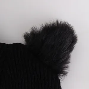 Close-up of a black knit beanie featuring a fluffy pom-pom detail and thick texture