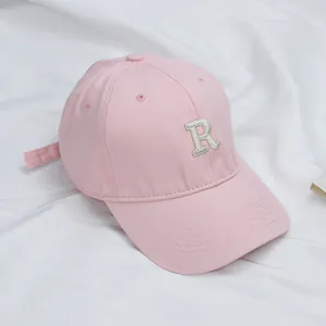 Pink cotton baseball cap with embroidered letter R on a clean white textured fabric