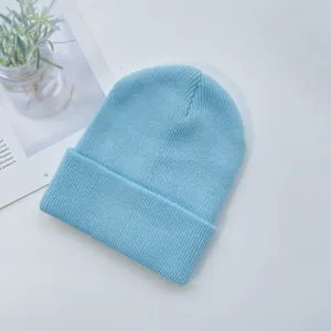 Détail du bonnet en maille côtelée bleu clair avec large revers sur fond blanc épuré