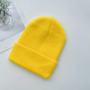 Détail du bonnet en maille jaune vif avec large revers sur fond blanc minimaliste