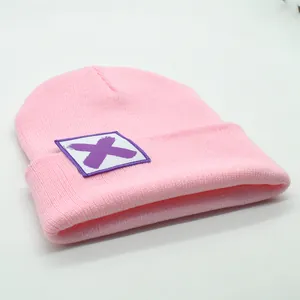 Detail der rosa Strickmütze mit quadratischem weißem Aufnäher und lila X-Grafikmuster