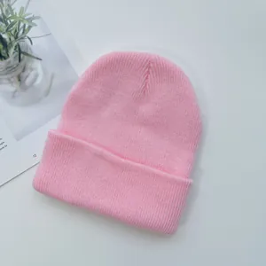 Light pink knitted beanie hat with a ribbed texture and folded cuff on a white background