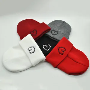 Detail of winter knit beanies in multiple colors with heart embroidery and ribbed texture