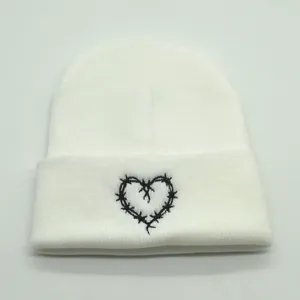Close-up of white knit beanie featuring black barbed wire heart embroidery detail
