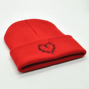 Winter red knitted beanie with heart-shaped barbed wire embroidery in a minimalist style