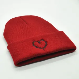 Detail of red cuffed beanie featuring black heart embroidery with thorn design