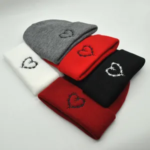Detailed close-up of barbed wire heart embroidery on various colored winter knit beanies