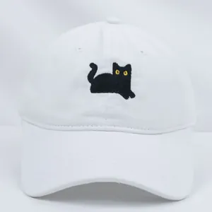 Dettaglio del ricamo gatto nero su berretto in cotone bianco con occhi gialli vivaci