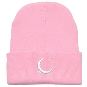 Berretto rosa in maglia con ricamo a luna e stelle bianche su sfondo bianco pulito