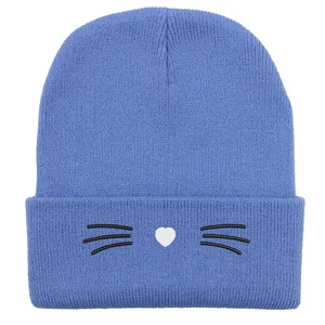 Dettaglio del berretto in maglia azzurro con baffi di gatto neri e cuore bianco ricamato