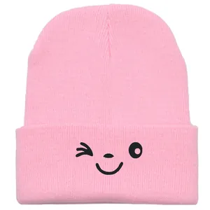 Pink knitted beanie for women featuring a cute embroidered smiley face on the front fold