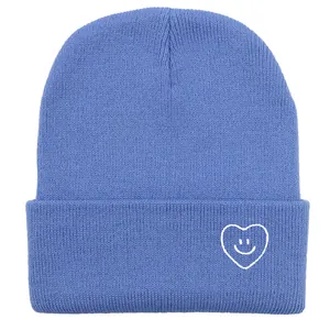 Détail de bonnet tricoté bleu clair avec motif brodé de visage souriant en cœur