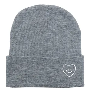 Détail du bonnet en maille grise avec broderie de cœur souriant blanc sur le revers