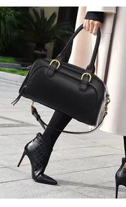 Detail of a black leather bowling bag with gold hardware held by a woman in a trench coat