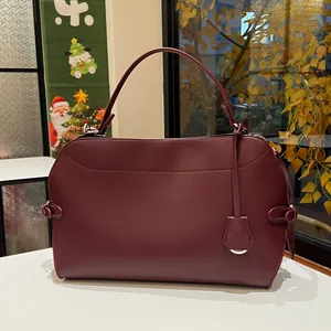 Detail view of burgundy leather handbag with round handle and decorative clochette pendant