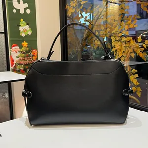 Detail view of the black leather handbag featuring a sturdy handle and metallic buckles