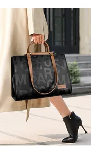 Close-up of black tote bag featuring embossed letters and contrasting brown leather straps
